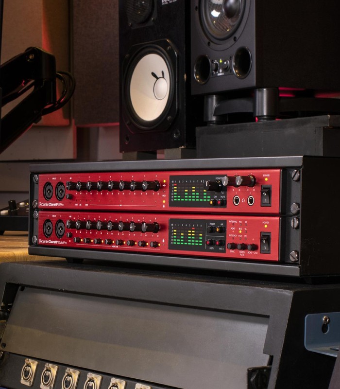 Focusrite Clarett+ OctoPre e 8Pre montados em rack num estúdio, com medidores LED e monitores visíveis.